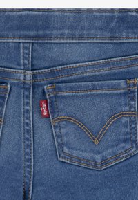 Donkerblauwe denim jeans met een achterzak met een rood Levi's label, contrasterende stiksels en een kenmerkend gebogen neklijnontwerp.
