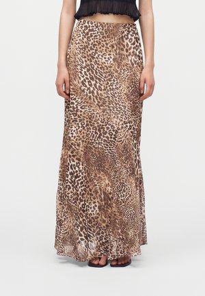 Mujer con una falda larga de estampado de leopardo en tonos marrón y beige combinada con un top negro corto sin mangas y sandalias negras.
