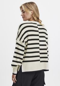 Gestreifter Pullover mit abwechselnd schwarzen und cremefarbenen Streifen, geripptem Saum und lässigem Schnitt mit überschnittenen Schultern, der ein strukturiertes Strickmaterial zeigt.