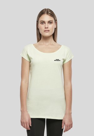 Femme aux cheveux raides porte un t-shirt jaune pâle à manches courtes avec le texte "THINK DIFFERENT." près de la poitrine gauche sur un fond uni.