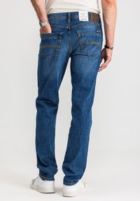 Niebieskie dżinsy z prostą nogawką, tylnymi kieszeniami, kontrastującym przeszyciem oraz skórzaną naszywką na pasku. Noszone z białymi trampkami.