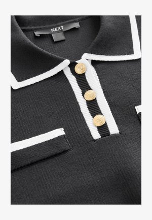 Schwarzes Poloshirt mit weißen Akzenten, einem gerippten Textil, drei goldenen Knöpfen und einem klassischen Kragen; beinhaltet zwei Brusttaschen.
