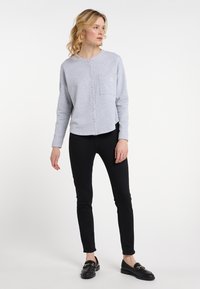 Šedá mikina s kulatým výstřihem, zapínáním na knoflíky a přední kapsou; v kombinaci s černými skinny džíny a černými mokasínami. Jednoduchý design, volný střih.
