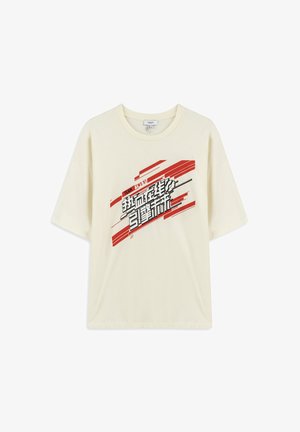 T-shirt crème à manches courtes en coton doux, avec un design graphique en texte noir et rouge audacieux sur le devant. Coupe décontractée et col rond.