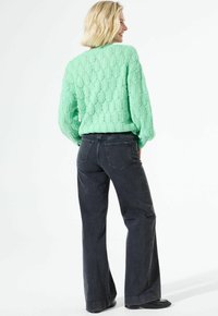 Pull tricoté vert menthe avec un motif texturé, associé à un jean large taille haute gris foncé et des chaussures plates noires.