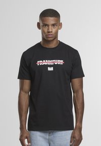 Zwarte t-shirt met een grafisch ontwerp waarin de tekst "FRANKFURT" in het rood en wit doorgehaald is, ronde hals, korte mouwen, gladde textuur.