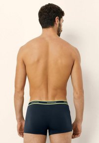 Boxeri din bumbac navy, cu o croială slim, având un elastic moale cu un accent galben și logo, priviți din spate.