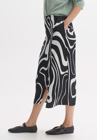 Zwart-wit gestreepte midi-skirt met een vloeiende uitstraling en zijslits, gemaakt van lichtgewicht stof. Gecombineerd met zwarte platte schoenen.