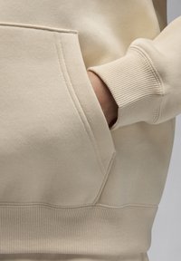Felpa beige con tasca a marsupio, polsini e orlo a costine, realizzata in un morbido tessuto testurizzato che enfatizza il suo design casual.