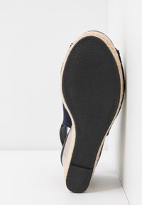 Semelle en caoutchouc noir d'une sandale compensée avec bordure en jute beige sur fond blanc d'une surface d'angle