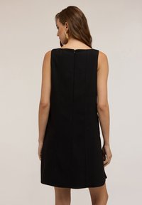 Vestido negro sin mangas con corte recto, que presenta una cremallera trasera, costuras verticales sutiles y una textura suave.
