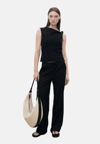 Haut sans manches noir avec un décolleté asymétrique et un design ajusté, associé à un pantalon noir ample et un sac hobo beige.