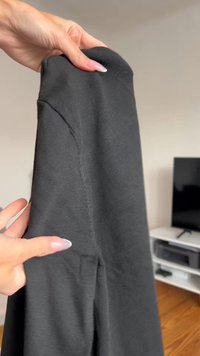 Čierny dlhý rukáv oblečenia držaný v ruke, ktorý zobrazuje textúrovanú látku, jemný lesk a viditeľné švy na rukáve.