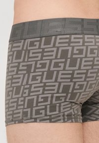 Szürke boxer alsók, amelyek ismétlődő világosszürke "GUESS" logó mintával rendelkeznek. Rugalmas derékpánt sima tapintással. Testhez simuló kialakítás.