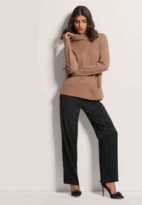 Brauner Strickturtleneck-Pullover mit Rippdetails, kombiniert mit schwarzen weiten Hosen mit subtilen Mustern. Schwarze High Heels.