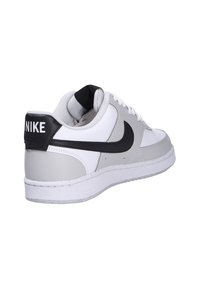Basket Nike blanche et grise avec logo swoosh noir et languette de talon noire avec texte Nike blanc, inclinée pour montrer les détails latéraux et arrière.
