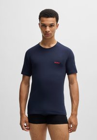 T-shirt ajusté bleu marine en matériau lisse, avec un col rond et un petit logo rouge "HUGO" sur le côté gauche de la poitrine.