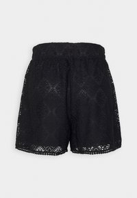 Shorts de encaje negro con cintura elástica, que presentan patrones intrincados y dobladillos con forma de concha, exhibiendo un diseño transparente y texturizado.