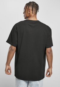T-shirt en coton noir à manches courtes, coupe décontractée et col rond. La vue arrière met en avant la texture lisse et les détails de couture.