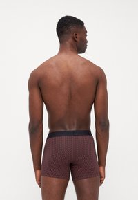 Herrarnas boxershorts i ett mönstrat tyg med en mörk midja, med en röd och marinblå zigzagdesign och en mjuk, slät yta.