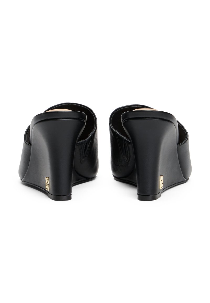 Schwarze Leder-Wedges mit einem geschwungenen Absatz, runder offenem Rücken und subtilen goldenen Hardwareakzenten. Glatte Textur und minimalistisches Design.