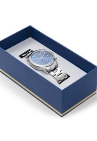 Silberne Metalluhr mit blauem Zifferblatt, Edelstahlarmband, präsentiert in einer blauen Box mit weißem Innenraum und goldenen Akzenten.