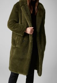 Kåbe i olivengrøn imiteret pels med store revers, dobbeltradet knaplukning og sidelommer, med en blød, tekstureret overflade.