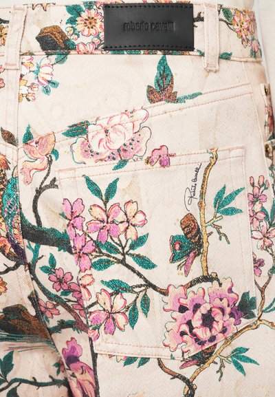 Blommönstrade denimjeans med en ljus krämfärgad bas. Har rosa blommor, gröna blad och en svart läderetikett med "roberto cavalli."