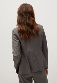 Grijze op maat gemaakte blazer met een enkele vent aan de achterkant, gemaakt van gladde stof, met lange mouwen en een klassieke pasvorm.