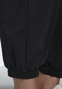 Svarta joggingsbyxor med elastiska avslut och texturerad tyg. Har en slät design med en något skrynklig yta.