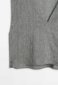 Haut en tissu gris tissé avec une finition texturée, présentant un décolleté en V et un ourlet légèrement courbé. Aucun motif ou détail matériel remarquable.