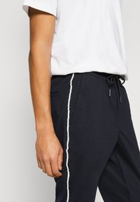Pantalons de jogging marine en tissu doux, avec un taille élastique à cordon de serrage, des poches latérales et des bandes latérales blanches contrastées.
