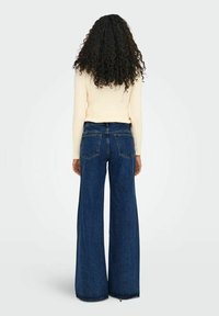 Vaqueros de talle alto y pierna ancha en denim azul oscuro. Presentan un diseño clásico de cinco bolsillos y detalles de costura sutiles. Textura suave.