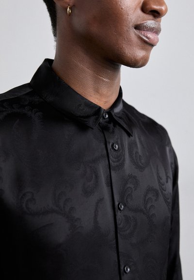 Camicia nera con finitura lucida, caratterizzata da un sottile motivo vorticoso, abbottonatura e colletto. Tessuto liscio e vestibilità su misura.