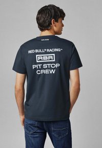 Laivansinis puuvillapaita, jossa on valkoista tekstiä. Etupuolella lukee "PEPE JEANS"; takana on "RED BULL RACING", "RBR" ja "PIT STOP CREW" lihavoituna.