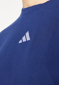Tamsiai mėlynas medvilninis T-shirt'as su apvalia iškirpte ir trumpomis rankovėmis. Viršutinėje kairėje krūtinės pusėje yra trys balti dryžiai.