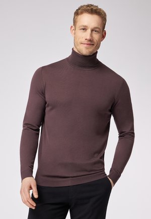 Rollkragenpullover in dunklem Mauve, gerippte Textur, schlanker Schnitt, lange Ärmel und ein enganliegender Kragen. Getragen über dunklen Hosen.