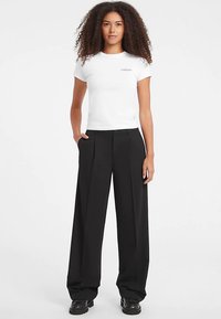 Tricou alb ajustat cu mâneci scurte și pantaloni negri cu talie înaltă, cu croială largă. Poartă cizme negre masive. Design simplu și textură fină.