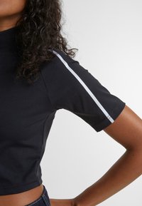 Svart kortärmad topp med hög halsringning. Har en smal vit rand längs axeln. Slät tyg med en åtsittande design.