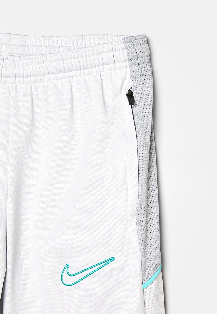 Pantalons de sport gris et blanc avec taille élastique, poche latérale avec zip et logo swoosh turquoise à l'avant. Panneau latéral texturé.