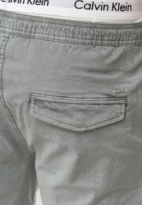 Shorts en coton gris avec une taille élastique arborant un logo "Calvin Klein". Comprend une poche arrière avec un rabat rectangulaire.