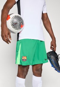 Grønne fodboldshorts med Barcelona-logo, parret med en hvid skjorte, sorte og blå fodboldstøvler samt en mønstrede fodbold.