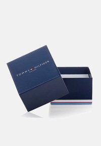 Scatola regalo di cartone blu con coperchio, presenta il logo "TOMMY HILFIGER" in argento sulla parte frontale e una striscia di accento rossa, bianca e blu nella parte inferiore.
