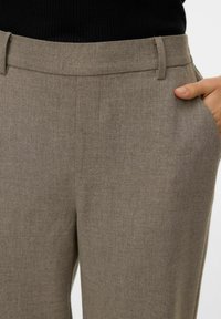 Beežid kohandatud püksid, millel on sile, tekstuuriga viimistlus, küljetaskud ja keskmise kõrgusega vöökoht. Nähtav on peen õmblusdetail.