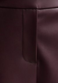 Burgundy leather pants with a smooth texture, featuring a side pocket and subtle seam detailing.