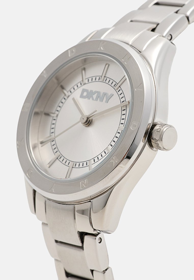 Silberne DKNY-Uhr mit einem Armband aus Edelstahl, rundem Zifferblatt und minimalistischer silberner Zifferblattgestaltung mit Stundenmarkierungen und Markenlogo.