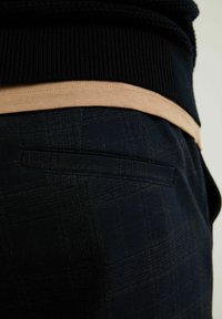 Marinrandiga byxor med texturerat tyg. Inkluderar ett beige midjeband och detalj på bakfickan, som framhäver skräddarsydd design.