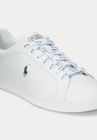 Valge Polo tennisejalanõu Polo logoga küljel ja kaubamärgiga paeladega, millel on madala lõikega disain ja puhas, sile viimistlus.