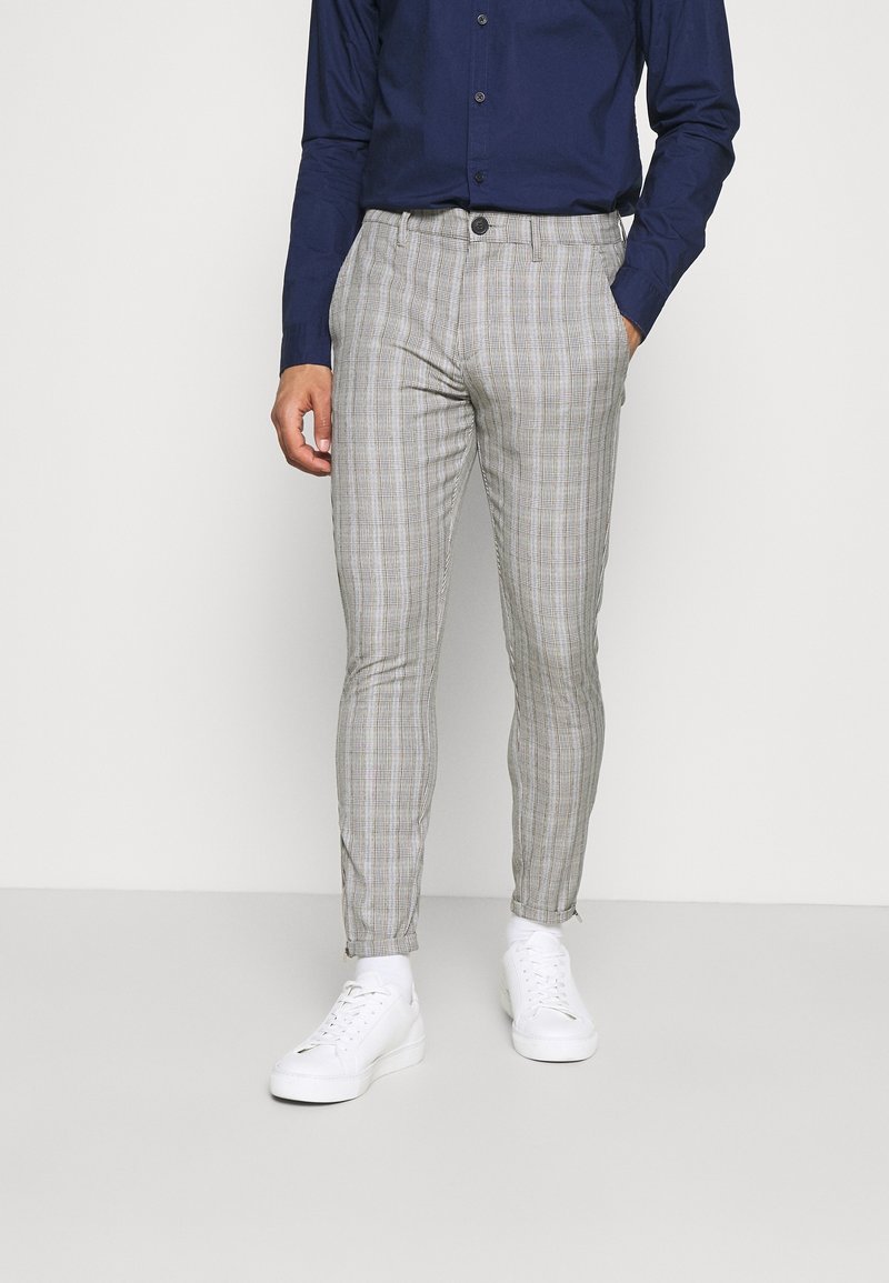 Grå rutig byxa med slim fit. Har en knappstängning och textil med struktur. Matcher med vita sneakers och en mörkblå skjorta.