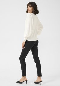 Bílý top s balónovými rukávy, vysokým výstřihem a knoflíkovými detaily na zádech, v kombinaci s černými skinny džíny a černými lodičkami na vysokém podpatku.